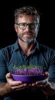 Mature Caucasian man with glasses and gray hair holding purple bowl of fresh microgreens against dark background, demonstrating healthy eating and urban farming.