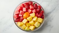Fresh cut watermelon, pineapple and strawberries in glass bowl on marble background, colorful tropical fruit mix for healthy breakfast or dessert.