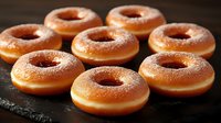 Fresh glazed donuts with sugar coating arranged on dark slate surface for bakery menu and breakfast concept.