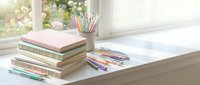 Stack of colorful books with pencils and art supplies on bright windowsill desk creating inspiring study workspace for creative learning and education.