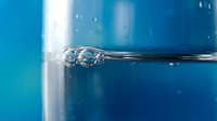 Clear water bubbles floating in blue liquid with transparent glass surface creating refreshing aquatic atmosphere for wellness and purity concepts.