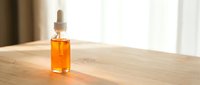 Amber glass dropper bottle with golden serum on wooden surface in bright natural light for skincare and wellness products.