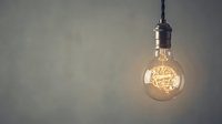 Vintage Edison bulb hanging from ceiling with warm glowing filament against neutral wall background for interior design and lighting concepts.