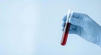 Gloved hand holding a test tube with red blood sample against light blue background for medical and laboratory use.