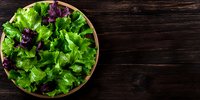Fresh green and purple lettuce leaves in wooden bowl on dark rustic wooden background with copy space. Top view of healthy organic salad greens.