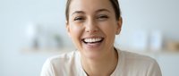 Young professional woman laughing joyfully in modern office environment, expressing happiness and positive emotions during work day.