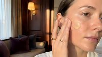 Young woman applying facial cream in luxury hotel room during skincare routine with warm ambient lighting and elegant interior background.