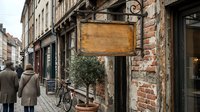 Vintage wooden signboard hanging on ornate metal bracket outside historic brick building on charming European street with pedestrians and bicycle.