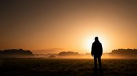 Silhouette of person standing in misty field at golden sunrise with warm orange sky and peaceful countryside landscape for meditation and inspiration.