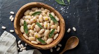 White beans with breadcrumbs and herbs in wooden bowl on dark slate background. Healthy vegetarian protein meal with rustic kitchen styling and natural lighting.