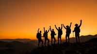 Silhouettes of diverse group of people with raised arms celebrating success on mountain peak at sunset, representing achievement, teamwork, and outdoor adventure.