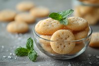 Homemade sugar cookies in glass bowl garnished with fresh mint leaves and sprinkled with crystal sugar on dark concrete surface, macro food photography.
