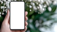 Mockup of smartphone with blank white screen held in female hand against blurred white flowers and green foliage background for app or website presentation.