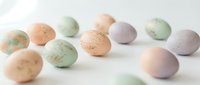 Pastel colored Easter eggs in soft green, peach and lavender hues scattered on white background for spring holiday decorations and seasonal crafts.