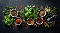 Fresh herbs and aromatic spices arranged on dark slate background with mortar and pestle for culinary cooking and seasoning preparation.