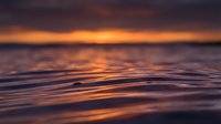 Tranquil ocean waves at sunset with golden orange light reflecting on water surface creating peaceful seascape atmosphere for meditation and relaxation.