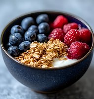 Fresh yogurt bowl with granola, blueberries and raspberries in dark ceramic bowl. Healthy breakfast with natural ingredients and fresh berries.
