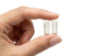 Hand holding two small transparent glass vials with cork stoppers isolated on white background for laboratory research and scientific experiments.