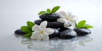 Zen spa composition with stacked black massage stones, delicate white jasmine flowers, and fresh green leaves on reflective surface.