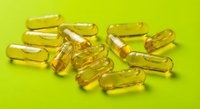 Golden yellow vitamin capsules scattered on bright green background for health and wellness supplement advertising.
