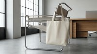 Blank canvas tote bag mockup on modern office chair in minimalist workspace with natural lighting for branding and design presentation.