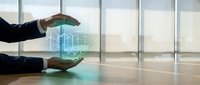 Businessman holding glowing holographic building model between hands in modern office with windows, representing real estate technology and property development innovation.