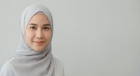 Young Muslim woman wearing light gray hijab smiling warmly at camera against neutral background for professional headshot and diversity content.