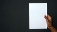 Hand holding blank white paper sheet against dark background, suitable for mockups, presentations, advertising campaigns, and design templates.