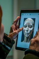 African American hands holding tablet displaying facial recognition wireframe model, demonstrating modern biometric security and AI technology application.
