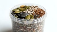 Assorted seeds and nuts in glass jar including pumpkin seeds, sunflower seeds, flax seeds for healthy snacking and cooking ingredients on white background.