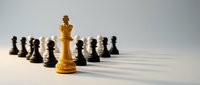 Golden chess king piece standing prominently in foreground with black pawns arranged in background, symbolizing leadership and strategic thinking.