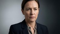 Middle-aged woman with short brown hair and fair complexion wearing dark blazer over striped shirt, serious expression, studio portrait for corporate or professional use.
