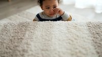 Young child with curly dark hair and medium skin tone crawling on beige carpet indoors, wearing casual clothing. Developmental milestone moment.