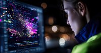 Young Asian male programmer analyzing data visualization on computer screen with colorful particle effects and code, working late at night in dark office environment.