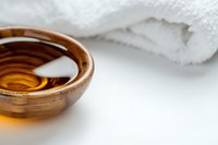 Wooden bowl with golden massage oil and white towel on light background, wellness and spa concept for aromatherapy and relaxation treatments.