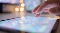 Hand touching digital tablet screen with colorful app icons and bokeh lights in background creating modern technology interaction scene.