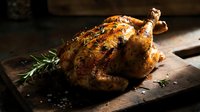 Golden roasted whole chicken with herbs on wooden cutting board, perfectly cooked poultry for holiday dinner or family meal preparation.