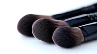 Professional makeup brushes with soft black bristles arranged in diagonal composition on white background, close-up view showing texture and quality details.