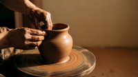 Skilled potter's hands shaping clay vessel on spinning wheel in warm studio light. Traditional ceramic craftsmanship and artisan pottery making process.