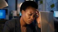 Stressed African American businesswoman working late at office computer experiencing headache and fatigue from overtime work pressure.