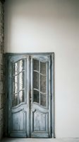 Vintage weathered blue French doors with glass panels against white wall in rustic interior space for home decor and renovation projects.