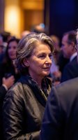 Elegant senior woman at formal business event with crowd in background, professional networking gathering with warm lighting atmosphere.