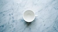 Empty white ceramic cup on marble surface with blue veining, overhead view, minimalist composition for beverage, kitchen, and lifestyle design projects.