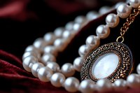 Pearl necklace with vintage bronze pendant on dark red velvet background, elegant jewelry composition with selective focus and soft lighting effect.