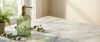 Green glass soap dispenser on marble bathroom counter with eucalyptus leaves and natural sunlight creating peaceful spa atmosphere for home decor.