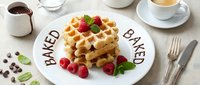Stack of golden waffles with fresh raspberries and mint on a white plate, chocolate sauce and coffee cup on linen background.