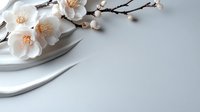 Delicate white plum blossoms with golden stamens on brown branches laying on curved white ceramic plate against soft gray background, creating minimalist composition.
