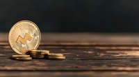 Golden Monero cryptocurrency coin standing upright with smaller coins on rustic wooden surface against dark background, symbolizing digital finance.