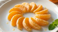 Fresh peeled mandarin orange segments arranged in a circle on a white plate with mint leaves, showcasing vibrant citrus fruit for food and nutrition concepts.