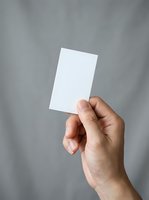 Hand holding blank white card against neutral gray background, suitable for business card mockups, branding presentations, and corporate identity designs.